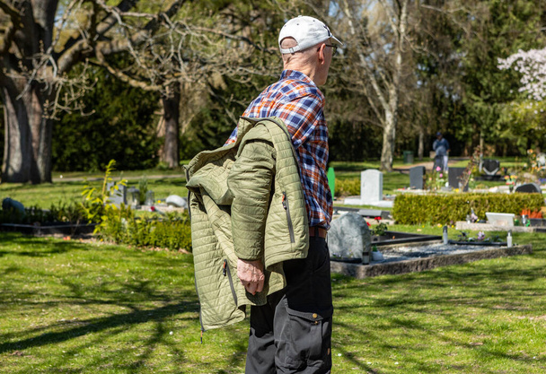 Old man taking jacket of at cemetery - Fotó, kép