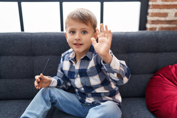 Adorable caucasian boy saying hello with hand sitting on sofa at home - Photo, Image