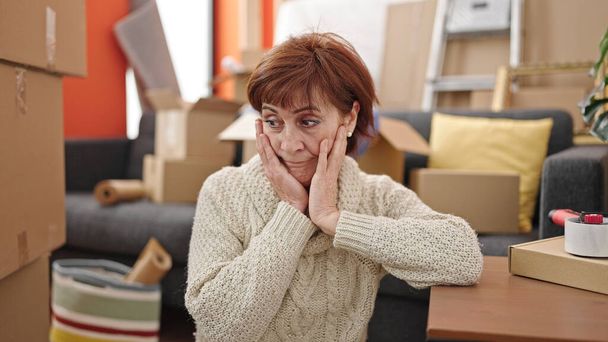 Зріла іспаномовна жінка сидить на підлозі, дивлячись навколо втомленого в новому будинку
 - Фото, зображення