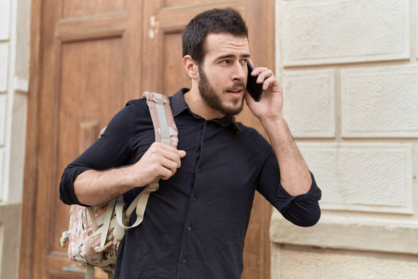 Genç İspanyol adam akıllı telefondan konuşuyor. Sokakta sırt çantası takıyor. - Fotoğraf, Görsel