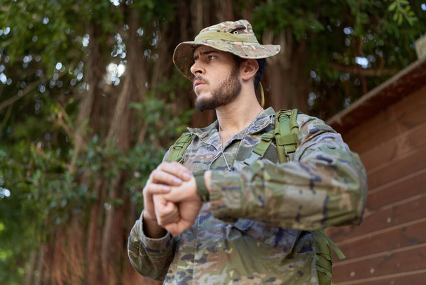 Mladý hispánec muž na sobě voják uniforma hledá hodinky v parku - Fotografie, Obrázek