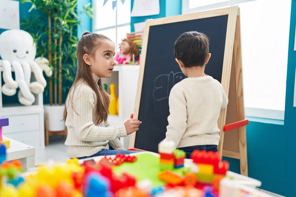 Adorable boy and girl preschool students drawing on blackboard at kindergarten - Foto, imagen