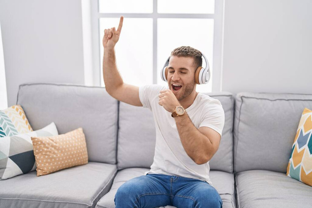 Young caucasian man listening to music singing song at home - Foto, afbeelding