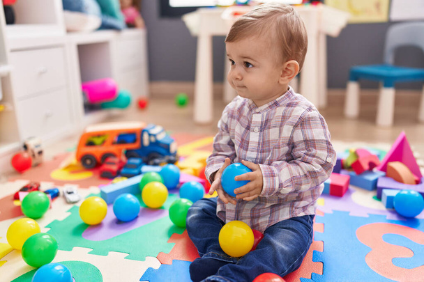Adorable caucasian boy playing with balls sitting on floor at kindergarten - Photo, Image