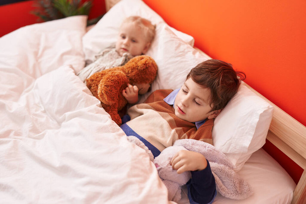 Adorable boy and girl hugging teddy bear sleeping on bed at bedroom - Photo, Image