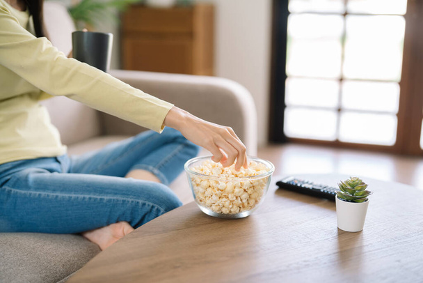 Asijská žena Sledování smart TV a pomocí dálkového ovladače Ruční držení televizního zvuku dálkové ovládání doma s popcornem - Fotografie, Obrázek