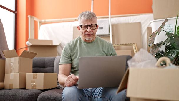 Homem de cabelos grisalhos de meia idade usando laptop com expressão séria em nova casa - Foto, Imagem