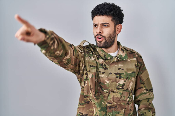 Arab férfi álcázott katonai egyenruhában, ujjal mutogatva meglepett előre, nyitott szájjal, csodálkozó arckifejezéssel, valami az elején.  - Fotó, kép