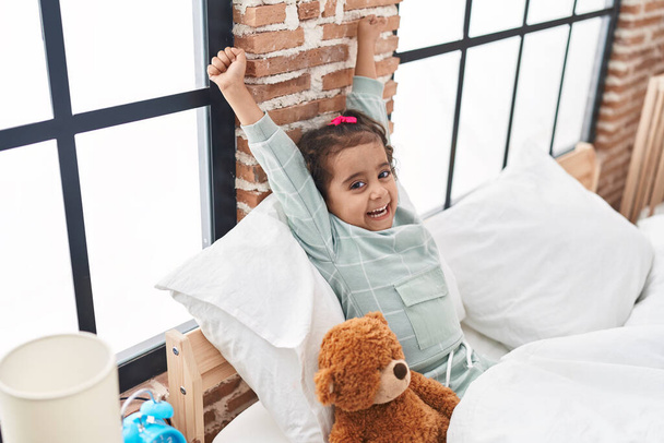 Adorable hispanic girl waking up stretching arms at bedroom - Photo, Image