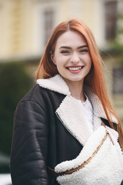 una chica pelirroja con una chaqueta de cuero. mujer alegre con el pelo rojo largo posa para un fotógrafo. - Foto, Imagen