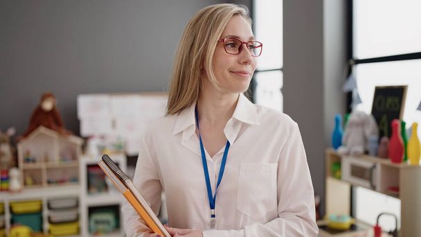 Mladá blondýnka žena předškolní učitel úsměv sebevědomí držení knih ve školce - Fotografie, Obrázek