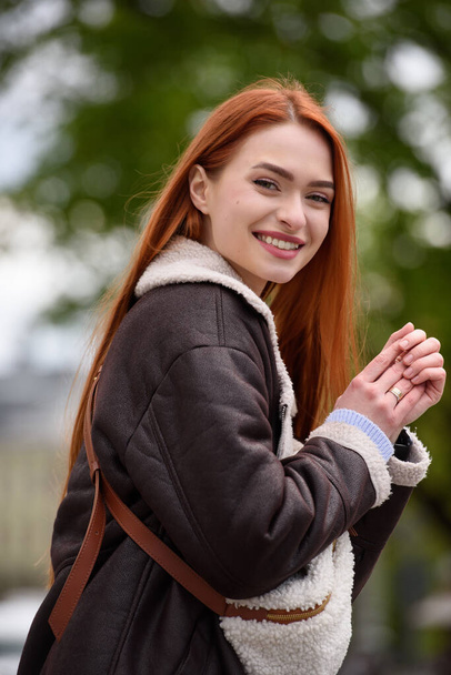 a red-haired girl in a leather jacket. cheerful woman with long red hair poses for a photographer. - Foto, Bild