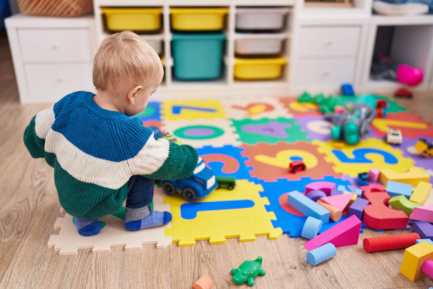 Adorable caucasian boy playing with car toy sitting on floor at kindergarten - Foto, Imagem