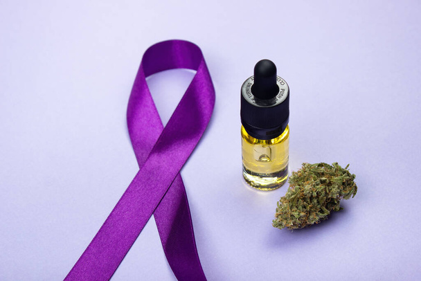 Glass bottle with cbd oil extract.  Nearby is a dry bud of medical marijuana.  Epilepsy day symbol from the purple ribbon on the left.  On a purple background.  Alternative treatments for epilepsy - Photo, Image