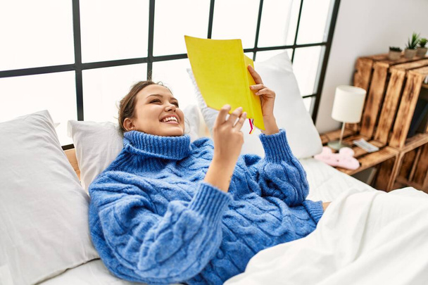 Jovem bela mulher hispânica lendo livro deitado na cama no quarto - Foto, Imagem