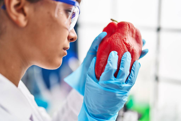 Young beautiful hispanic woman scientist examining red pepper at laboratory - 写真・画像