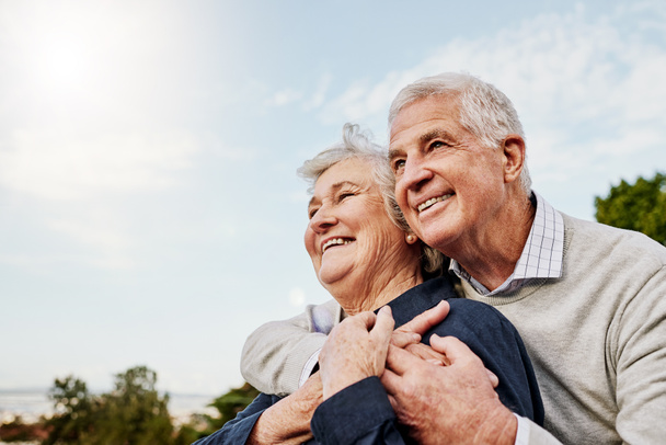 Himmel, älteres Paar und Umarmung im Freien oder glücklich im Ruhestand oder Mann und Frau in der Natur. Ältere Männer und Frauen lächeln im Urlaub oder Senioren pflegen und umarmen sich oder verabreden sich im Park zur Romanze. - Foto, Bild