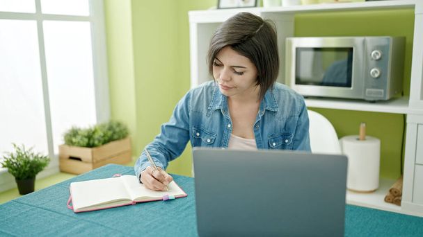 Jovem caucasiana usando laptop escrita no notebook em casa - Foto, Imagem