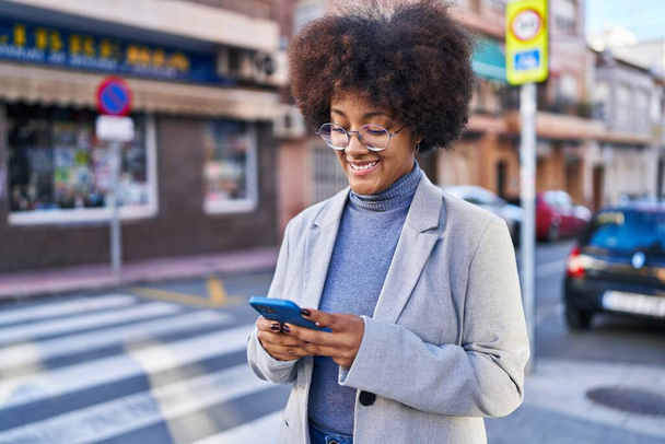 Afrikaans amerikaanse vrouw executive glimlachen zelfverzekerd met behulp van smartphone op straat - Foto, afbeelding
