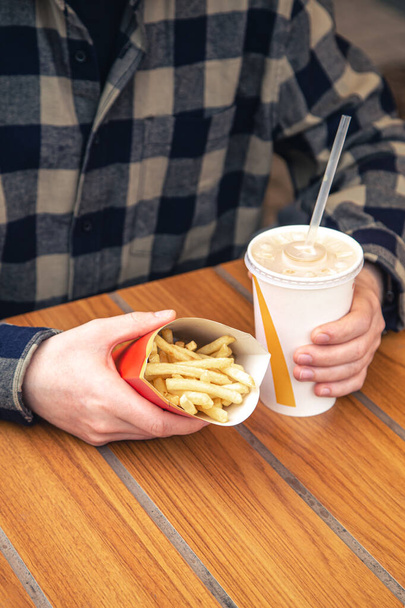 Close-up, batatas fritas e uma bebida em mãos masculinas em um café fast food, um lanche insalubre. - Foto, Imagem