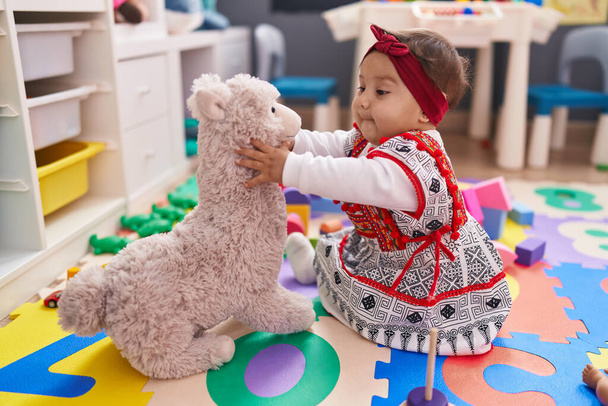 Adorable bebé hispano sonriendo confiado jugando con juguete en el jardín de infantes - Foto, imagen