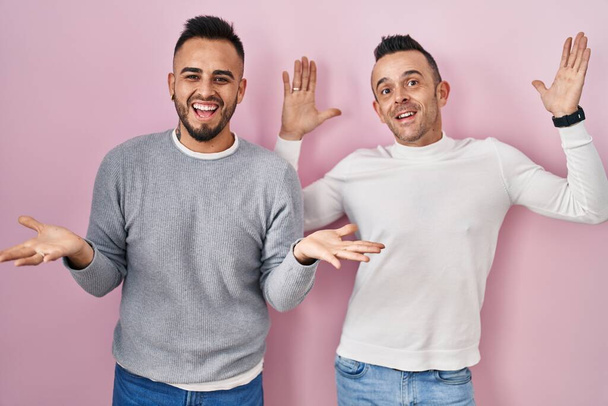 Homosexual couple standing over pink background celebrating crazy and amazed for success with arms raised and open eyes screaming excited. winner concept  - Fotoğraf, Görsel