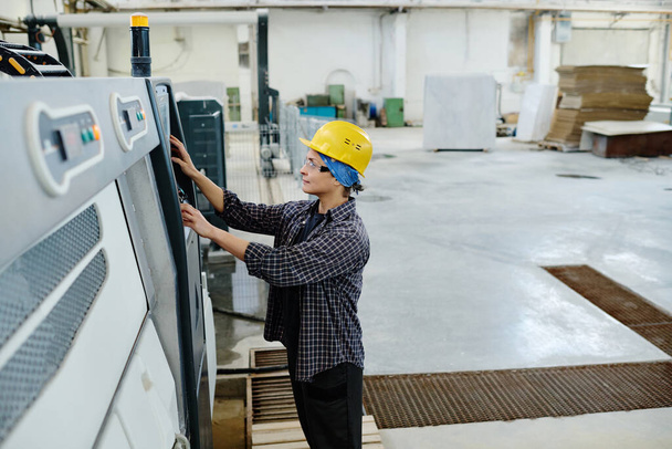 Високий кут зору працівника жінки в шоломі, що контролює роботу машини під час виробництва на заводі
 - Фото, зображення