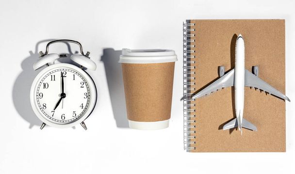 Alarm clock, paper cup, airplane model and notebook on white background, top view. Travel concept. - Photo, image