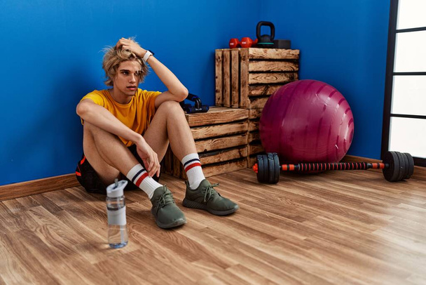 Fiatal szőke férfi fáradt ül a padlón a sportközpontban - Fotó, kép