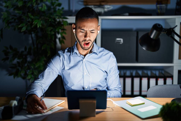 Молодой латиноамериканец, работающий ночью в офисе в шоке, выглядящий скептически и саркастично, удивленный с открытым ртом  - Фото, изображение