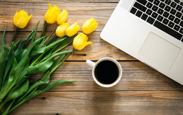 Laptop, eine Tasse Kaffee und ein Strauß Tulpen auf einem hölzernen Hintergrund, Draufsicht. - Foto, Bild