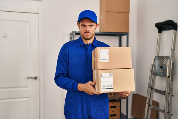 Jonge Spaanse man die werkt aan het verplaatsen van dienst houden dozen sceptisch en nerveus, fronsen boos vanwege het probleem. negatieve persoon.  - Foto, afbeelding