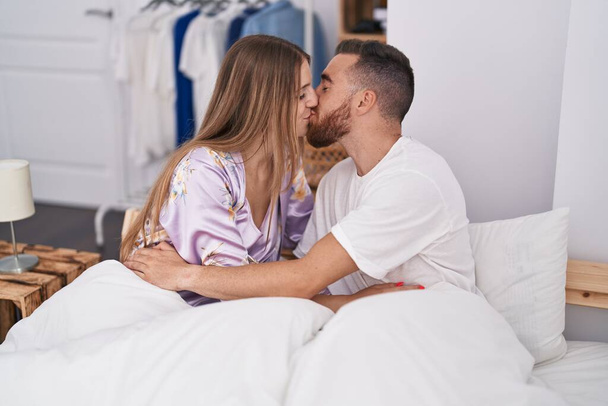 Άνδρες και γυναίκες κάθονται στο κρεβάτι και φιλιούνται στην κρεβατοκάμαρα. - Φωτογραφία, εικόνα