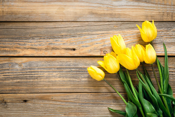 Voorjaarsachtergrond met gele tulpen op een houten achtergrond, bovenaanzicht, kopieerruimte. - Foto, afbeelding