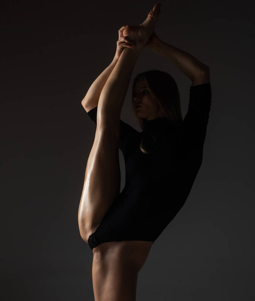 Leg-split. Flexible girl does gymnastic exercises for stretching. Beautiful sexy flexible woman demonstrates sexy flexible body. Flexibility stretching on black . Strong flexible female body - Zdjęcie, obraz