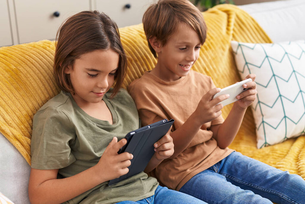 Adorable boys using smartphone and touchpad sitting on sofa at home - Foto, imagen
