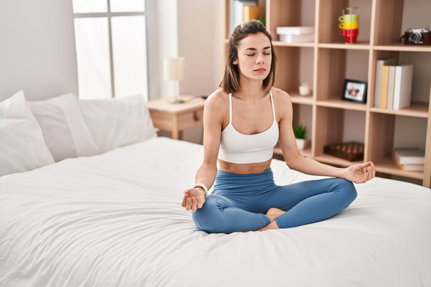 Giovane bella donna ispanica che fa esercizio di yoga seduto sul letto in camera da letto - Foto, immagini