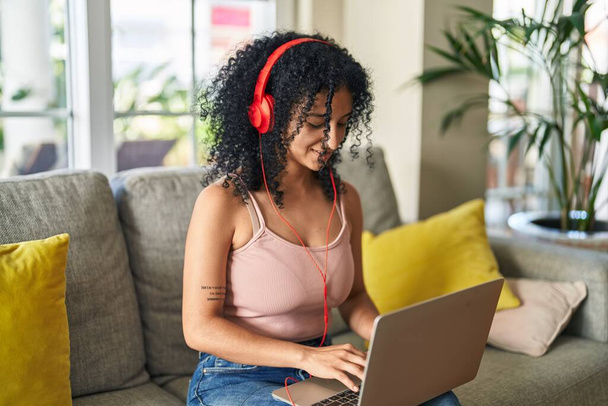 Jovem hispânica usando laptop e fones de ouvido sentados no sofá em casa - Foto, Imagem