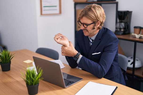 Young blond man business worker suffering for wrist pain working at office - Фото, изображение