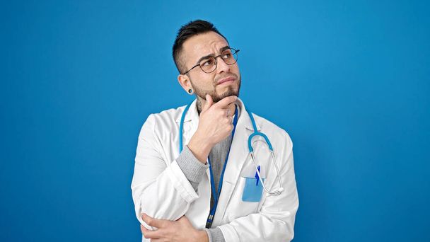 Лікар - латиноамериканець стоїть з сумнівом і думає над ізольованим синім фоном. - Фото, зображення