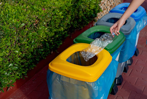 Zamknij się ręka wyrzucając plastikowe butelki recyklingu pojemnik śmieci sortowania śmietnika. Ręczne wkładanie plastikowego pojemnika na śmieci. Zmniejszyć pojemniki na odpady. Recykling plastikowych koszy na śmieci - Zdjęcie, obraz
