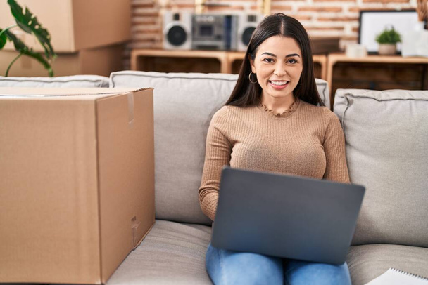 Young beautiful hispanic woman smiling confident using laptop at new home - Photo, Image