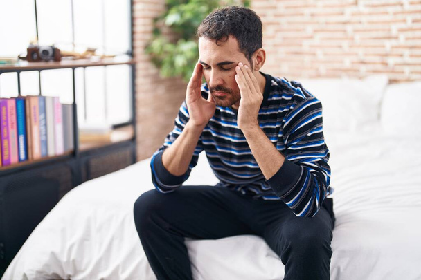 Young hispanic man stressed sitting on bed at bedroom - Photo, Image