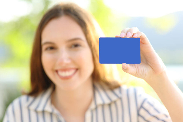 Happy woman showing blank credit card at camera in nature - Фото, изображение