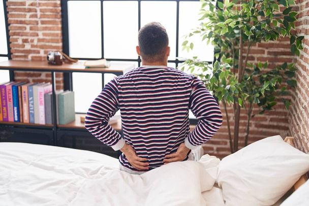 Молодий іспаномовний чоловік, який страждає травмою спини, сидячи в ліжку в спальні
 - Фото, зображення