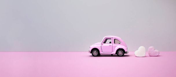 Kiev, Ukraine-January 2022: pink retro toy car on a gray background with heart-shaped marshmallows. Side view, space for text. - Foto, afbeelding