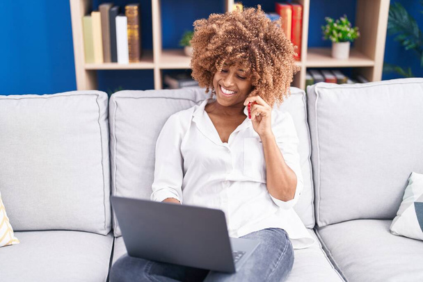 Αφροαμερικανή γυναίκα που μιλάει στο smartphone χρησιμοποιώντας φορητό υπολογιστή στο σπίτι - Φωτογραφία, εικόνα