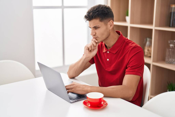 Nuori latino mies käyttää kannettavaa tietokonetta epäilevästi ilme kotona - Valokuva, kuva