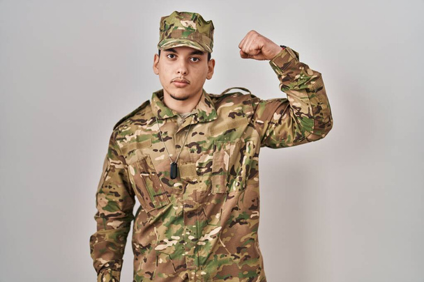 Jeune homme arabe portant uniforme de camouflage de l'armée personne forte montrant muscle du bras, confiant et fier de la puissance  - Photo, image