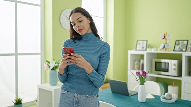 Nuori kaunis latino nainen käyttää älypuhelinta seisoo kotona - Valokuva, kuva